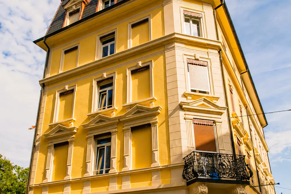 Die gelbe Fassade mit weinroten Fensterläden und schmiedeeisernem Balkon, von unten gesehen
